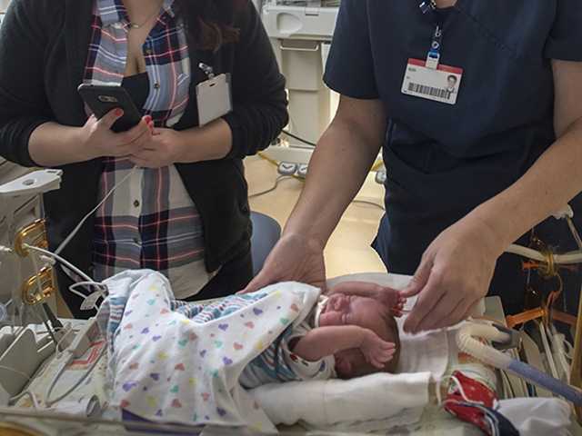 Nurse and mother standing over a baby in NICU