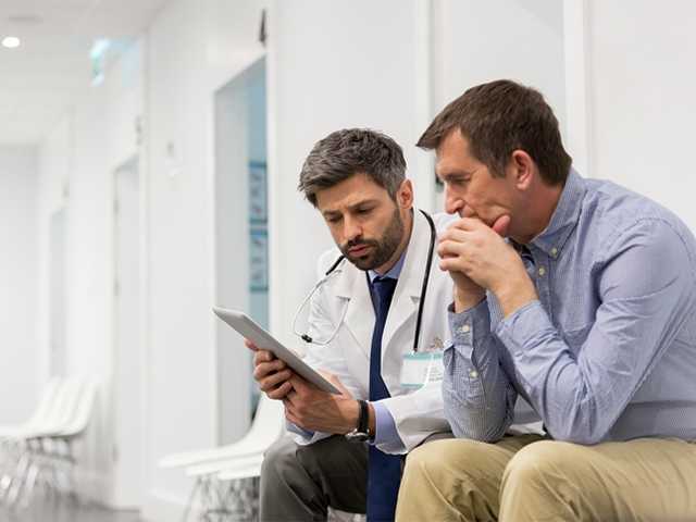 Healthcare provider showing man information on a tablet.